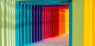 Covered-passageway made of slim-coloured rectangular pieces that form a box with the ground. The colors are in rainbow order, starting from green. Photo credit for Robert Katzki, Unsplash.